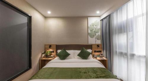a bedroom with a bed with two green pillows at GreenTree Inn Express Zhangjiagang Hexing Town Shazhou Professional Institue of Technology in Qiwei