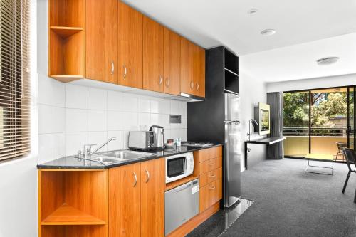 a kitchen with wooden cabinets and a sink at Sleek 1-Bed by Jubilee Park with Pool in Sydney