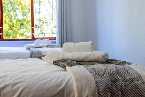 three white towels are stacked on top of a bed at Bed On Boucher in Durbanville