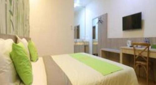 a bedroom with a bed with green pillows and a desk at Hotel Huswah Airport in Jakarta