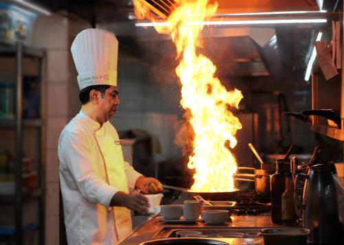 a chef cooking on a stove in a kitchen with flames at The Grandmark Dhaka in Dhaka