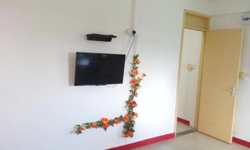 a television hanging on a white wall with flowers at Bano Tourist Residence - 650 meters from Grand Bay Beach in Grand Baie