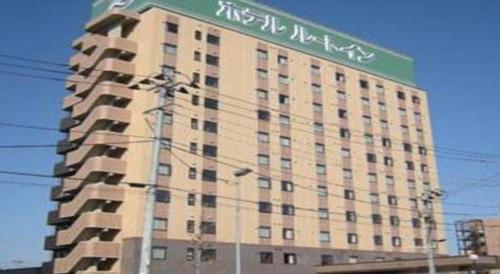 a large building with a green sign on top of it at Hotel Route Inn Furukawa Ekimae in Osaki