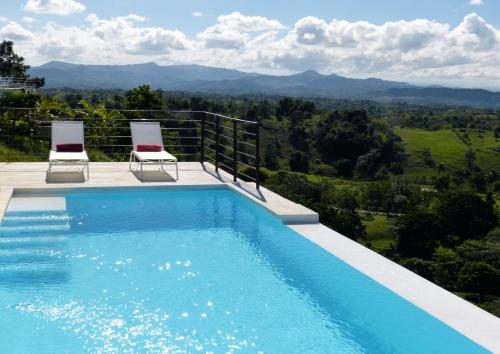 a swimming pool with two chairs and a view of the mountains at Villa Vertigo in Río San Juan