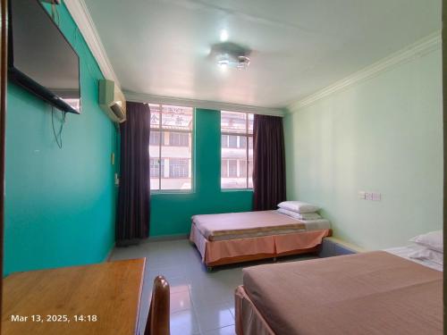 a room with two beds and a table and two windows at Hotel O Malaysia Hotel in Sandakan
