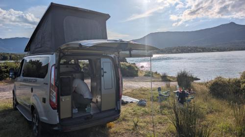 un camping-car garé à côté d'une masse d'eau dans l'établissement Van&Scoot, à Belgodère
