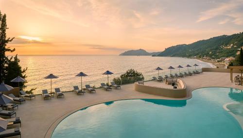 a pool with chairs and umbrellas next to the water at Alkyna Lifestyle Beach Resort - Adults Only in Agios Gordios