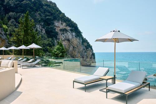 a patio with chairs and an umbrella and the ocean at Alkyna Lifestyle Beach Resort - Adults Only in Agios Gordios