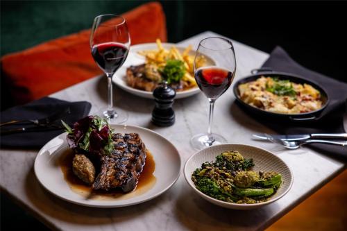 a table with plates of food and two glasses of wine at The Inchcolm by Ode Hotels in Brisbane