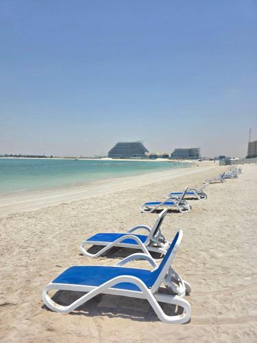 a row of blue and white lounge chairs on a beach at Seaview Escape Family Two-Room Apartment with Seaview in Ras al Khaimah