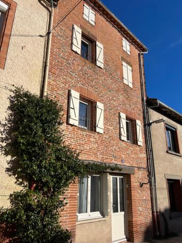 a red brick building with white windows and a tree at La petite maison dans le village in Lafrançaise
