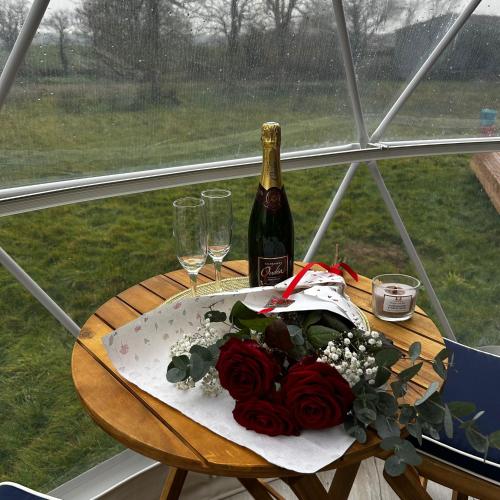 - une table avec une bouteille de vin et un bouquet de roses dans l'établissement Berry Dome, à Saint-Priest-la-Marche