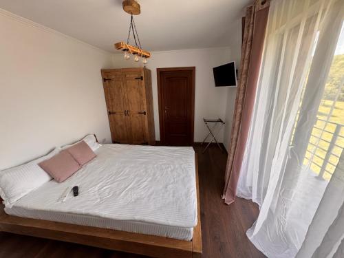 a bedroom with a bed with white sheets and a window at Pensiunea Lili’s House in Buchin