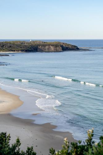 a beach with a small island in the water at The Bermuda - Oceanview Luxury in Ulladulla