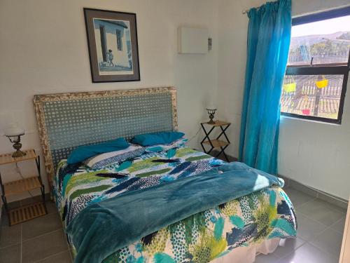 a bedroom with a bed with blue sheets and a window at Cozy Cottage in Hermanus