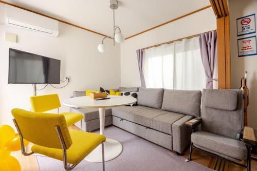 a living room with a couch and a table and yellow chairs at K's House Mizumoto in Tokyo
