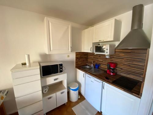 une petite cuisine avec des armoires blanches et un micro-ondes dans l'établissement Plage et commerces à 300 m tout à pied, idéal vacances, à Saint-Elme