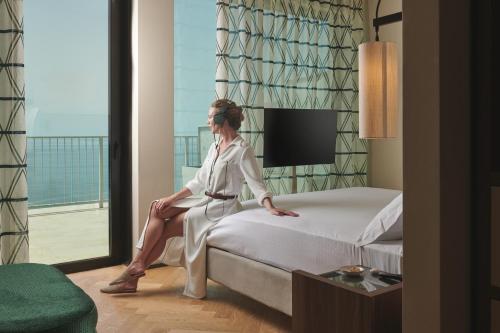 a woman sitting on a bed in a hotel room at Maximilian Suites in Trieste