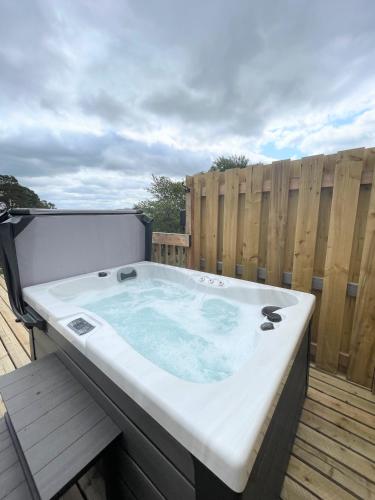 a hot tub on a deck with a wooden fence at Kaoglen - Bali Pod - Hot Tub -Cairngorms - Pitlochry in Kirkmichael