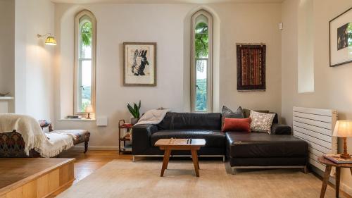 a living room with a black leather couch and windows at The Old Chapel in Painswick