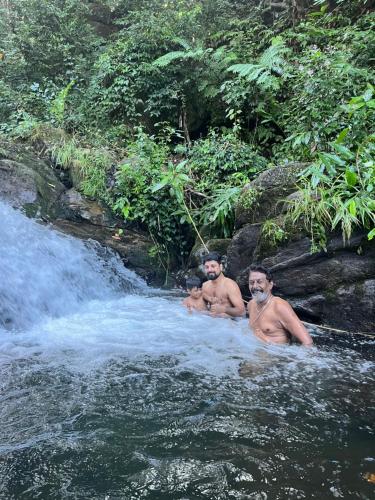 three men sitting in the water near a waterfall at Green and Green in Vagamon
