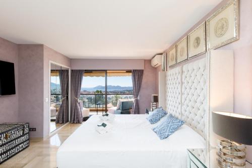une chambre avec un grand lit blanc avec une grande fenêtre dans l'établissement Les terrasses de victoria, au Cannet