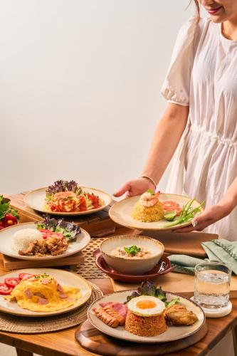 a woman standing in front of a table with plates of food at The Horizon Groove Hotel in Ban Khlong