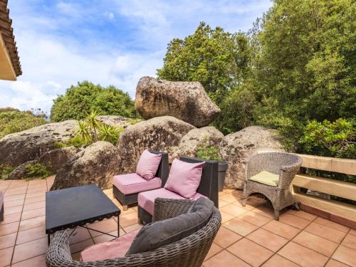 un patio avec des chaises et des tables en osier et des rochers dans l'établissement Holiday Home Villa Marina by Interhome, à Porto-Vecchio
