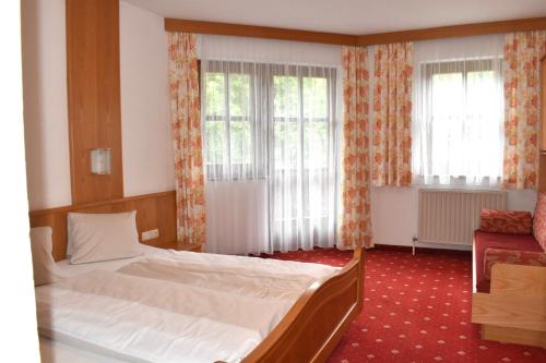 a bedroom with a large bed and two windows at Altachhof Hotel und Ferienanlage - Jokercard im Sommer inklusive in Saalbach Hinterglemm