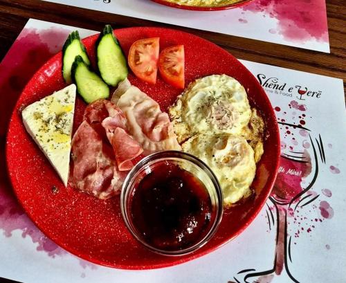 een rood bord met eten met vlees, eieren en fruit bij Moonlight Serenade in Korçë