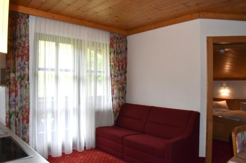 a living room with a red couch and a window at Altachhof Hotel und Ferienanlage - Jokercard im Sommer inklusive in Saalbach Hinterglemm