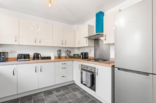 a kitchen with white cabinets and a refrigerator at Spacious 3-Bed Home, Parking, Garden, Sleeps 7 in Brettell Lane