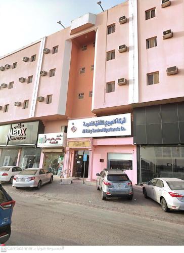 a pink building with cars parked in front of it at العييري للوحدات السكنيه المفروشة الاحساء 5 in Al Hofuf