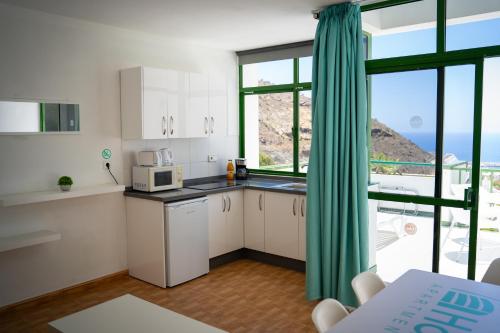 a kitchen with white cabinets and a large window at Apartamentos Halley in Puerto Rico de Gran Canaria