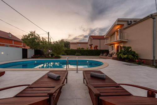 a swimming pool with wooden benches next to a house at Villa Sami ZadarVillas in Pristeg