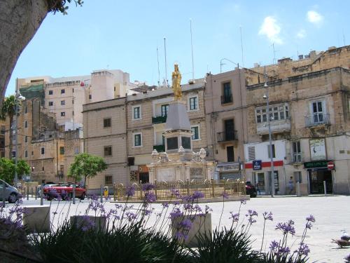 a statue in front of a building with purple flowers at Three Cities Apartments in Cospicua