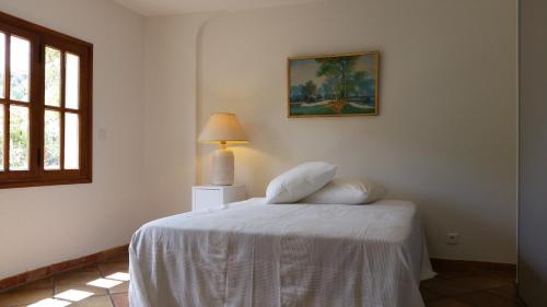 um quarto com uma cama com lençóis brancos e um candeeiro em Le Clos du Loup em La Colle-sur-Loup