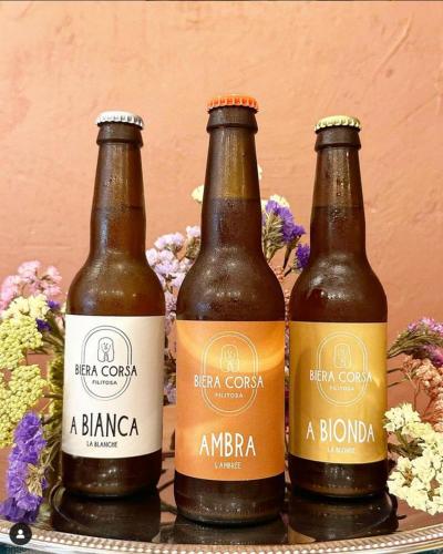 three bottles of beer on a table with flowers at Résidence de Filitosa - Le Torréen in Sollacaro
