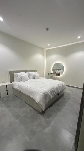 a white bedroom with a bed and a mirror at Royal Al Arfan Apartment in Muscat