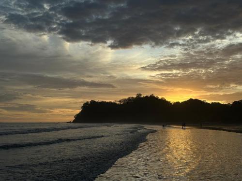 a sunset on a beach with people walking on the sand at Samara Tree House Inn in Sámara