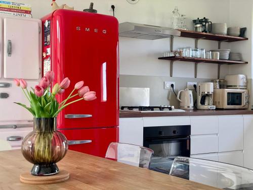un réfrigérateur rouge dans une cuisine avec un vase de fleurs dans l'établissement La Maison Rose - Côté Terre by Melrose, à Saint-Côme-de-Fresné