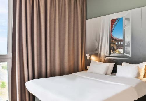 two white beds in a hotel room with a window at B&B HOTEL Les Herbiers in Les Herbiers