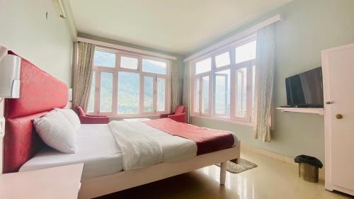 a bedroom with a bed and a tv and windows at Hotel Ocean & Meadows Open Terrace ! Mall Road Hotel ! in Manāli
