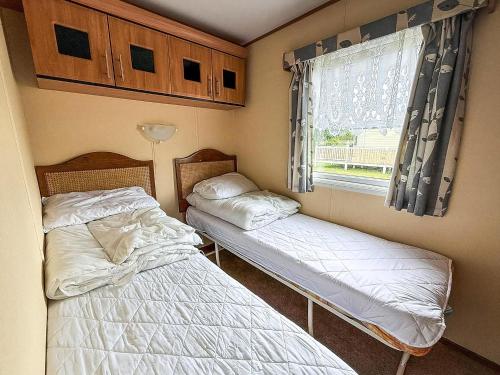 due letti in una piccola stanza con una finestra di Great Dog Friendly Caravan To Hire With Field Views In Norfolk Ref 10132B a Belton
