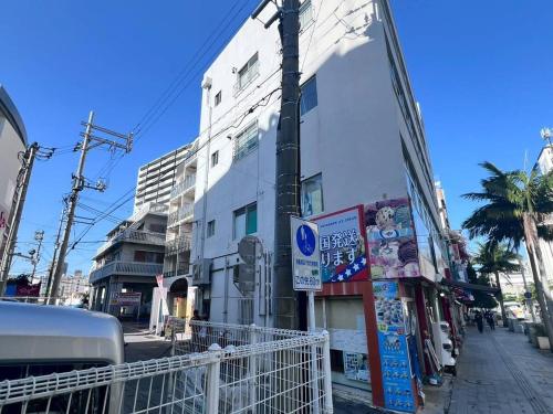 a white building on a street with a palm tree at Condominio Makishi Annesso in Naha