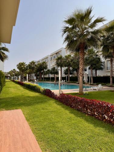 a swimming pool with palm trees and a building at Bright Apt with Balcony, WiFi, Parking and Pool Resort in Bouznika