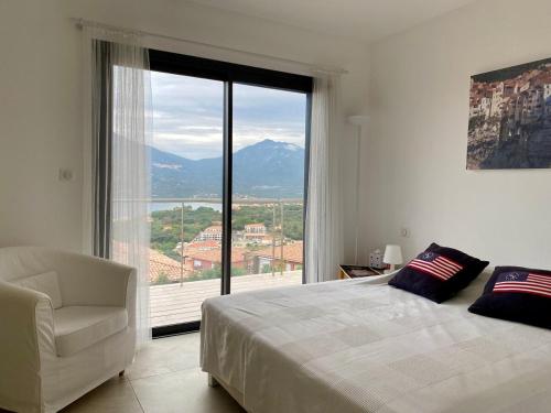- une chambre avec un lit, une chaise et une grande fenêtre dans l'établissement Villa Surplombant le Valinco, à Propriano