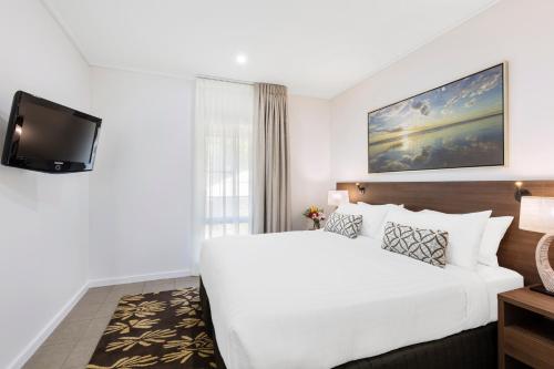 Habitación de hotel con cama blanca y TV en Oaks Cable Beach Resort, en Broome