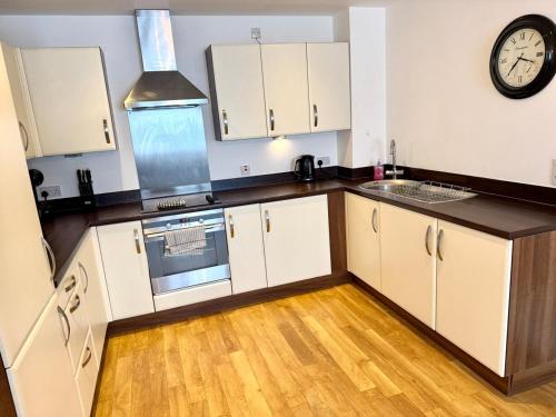 a kitchen with white cabinets and a clock on the wall at Charming 1BR Apartment In Heart of Cardiff Bay in Cardiff