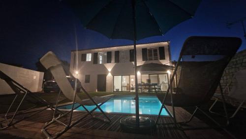 a pool with chairs and an umbrella in front of a house at La Villa des Lauriers in La Flotte